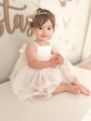 A baby sits wearing our Harper ivory baby flower girl romper, along with our Bryony baby floral headband.