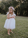 Harper tea length flower girl dress is worn by a young girl. The dress sits below her knees at shin length. She also wears our Luna flower crown, made up of light pink and purple flowers.