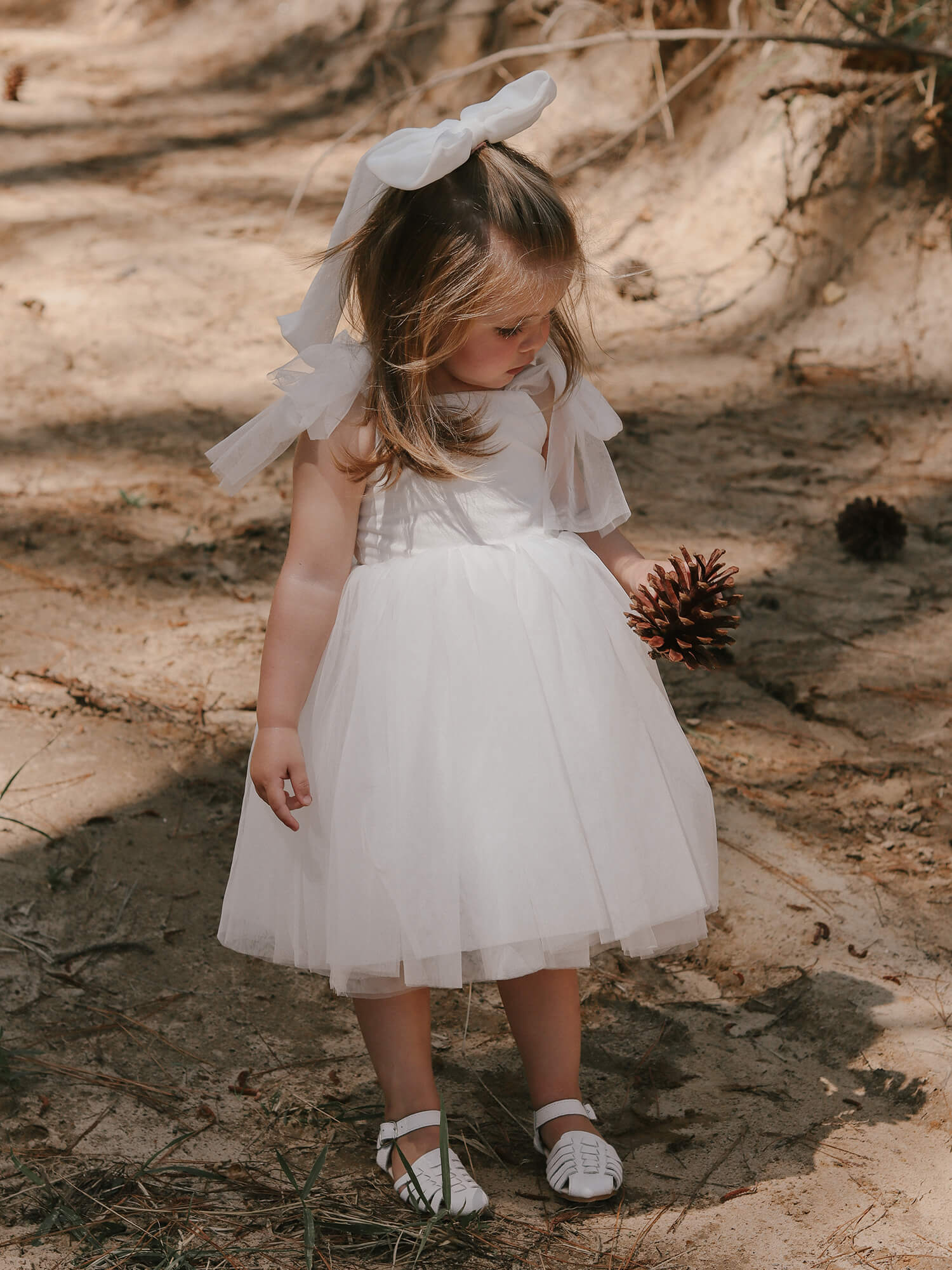Harper tea length flower girl dress is worn by a young girl. She also wears our classic large tulle bow in her hair. The tulle tie straps are tied in bows at her shoulders.