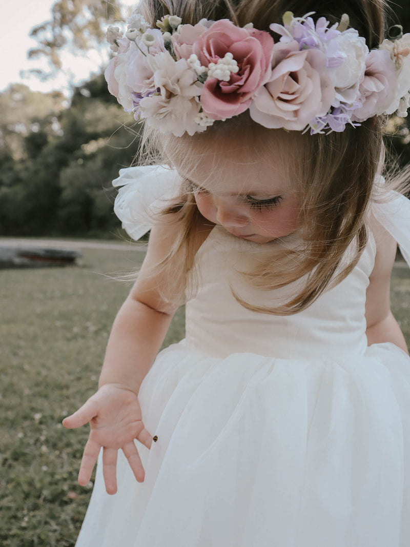 A toddler girl wears our Luna flower crown and Harper teal length flower girl dress. A ladybug has landed on the skirt of the dress and she looks at it.