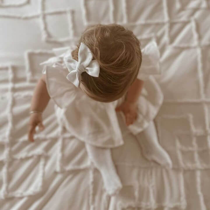 Baby girl wears our linen bow clip and Olive ivory linen romper.