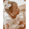 Baby girl wears our ivory linen bow clip in her hair, along with our Olive linen romper.