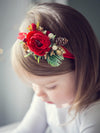 Chloe red Christmas floral headband shown on a toddler. A red centre peony surrounded with Christmas accents, including a mini pinecone and some gold. 