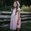 Rosie dusty pink flower girl dress is worn by a young girl, she also wears our matching tulle bow clip in her hair.
