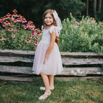 Rosie flower girl dress in dusty pink is worn by a young girl standing in a garden.