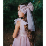Large dusty pink tulle bow is worn in a young girls hair, she also wears our matching Rosie dusty pink flower girl dress.