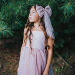 Rosie flower girl dress and tulle bow in dusty pink are worn by a young girl.