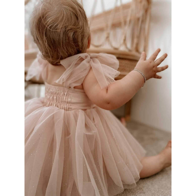 Rosie tulle baby romper with tulle bow straps is worn by a baby girl, in dusty pink.