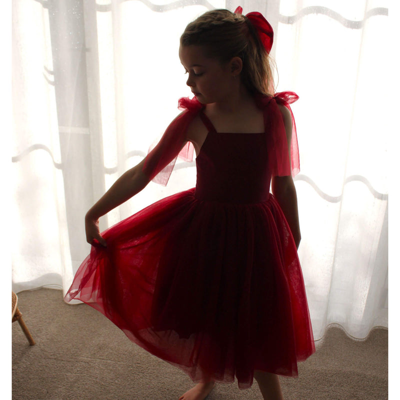 Rosie dress in wine crimson is worn by a young girl, showing the soft tulle tie straps and skirt. A beautiful girls Christmas dress.