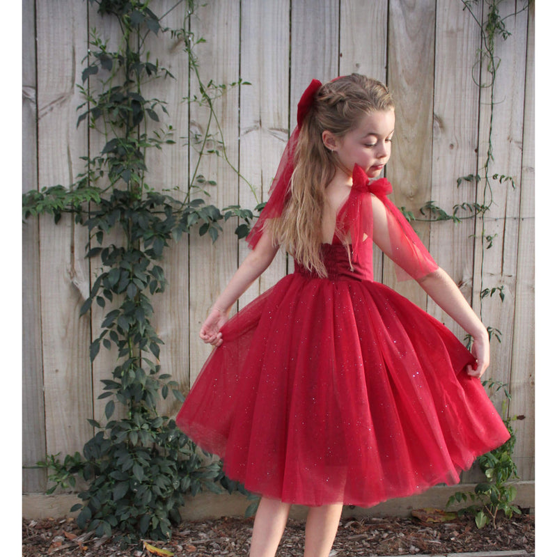 Rosie dress in crimson with glitter tulle is worn by a young girl. She also wears our matching tulle bow in crimson.